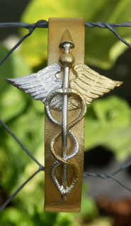 Armband met een band van zuiver goud, met daarop een Caduceus, die in zuiver goud en zuiver zilver is uitgevoerd. Het geheel is gematterd. 